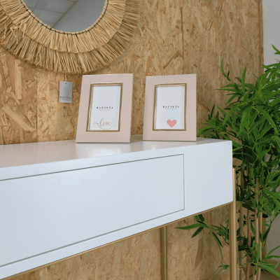 Dois porta-retratos beje com texto decorativo sobre mesa branca contra parede de madeira com planta verde ao lado