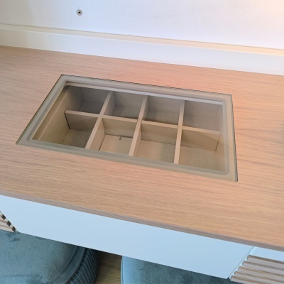 Caixa organizadora embutida em tampo de madeira clara com divisórias internas e tampa de vidro transparente