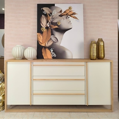 Aparador de madeira clara com portas brancas, decorado com jarras e quadro de mulher com flores
