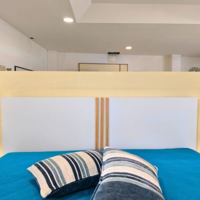 Cabeceira branca com detalhes de madeira clara, cama azul e almofadas às riscas em tons de azul.