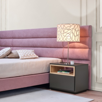 Cama estofada rosa claro com mesa de cabeceira preta e candeeiro com abajur branco