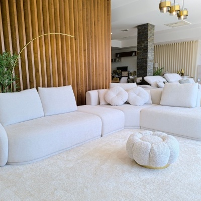 Sofá modular branco com almofadas e puff num ambiente moderno com parede de madeira.