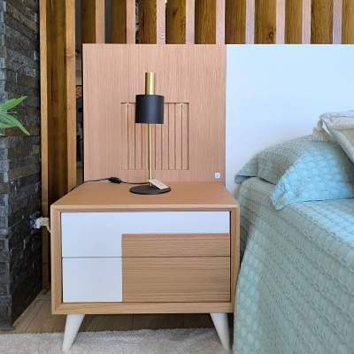 Mesa-de-cabeceira em madeira clara com candeeiro preto e dourado ao lado de cama com roupa azul