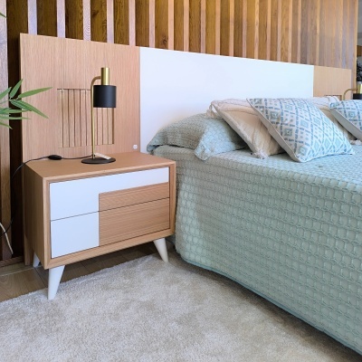 Mesa de cabeceira em madeira com gavetas branca e madeira, lâmpada preta e dourada, cama azul clara com almofadas e parede de madeira