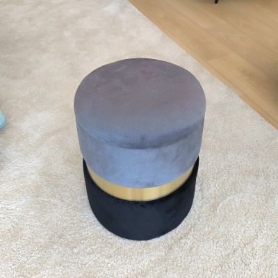 Pufe cilíndrico cinzento e preto com faixa dourada sobre tapete bege