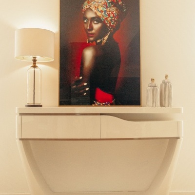 Consola branca moderna com candeeiro, garrafas decorativas e quadro de mulher com turbante colorido