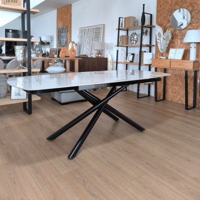 Mesa branca com pernas pretas cruzadas num ambiente decorado com móveis e objetos decorativos.