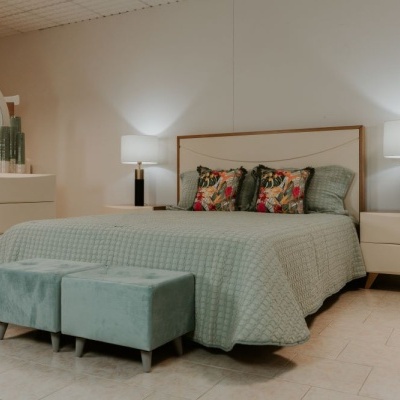 Quarto com cama, mesas de cabeceira, cómoda com espelho redondo e bancos verdes