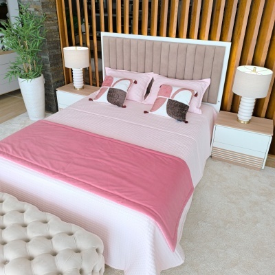 Cama de casal rosa com cabeceira estofada cinza claro e mesas de cabeceira brancas e candeeiros
