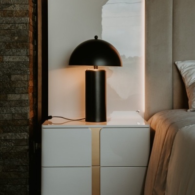 Mesa de cabeceira branca com candeeiro preto ao lado de cama com cabeceira estofada