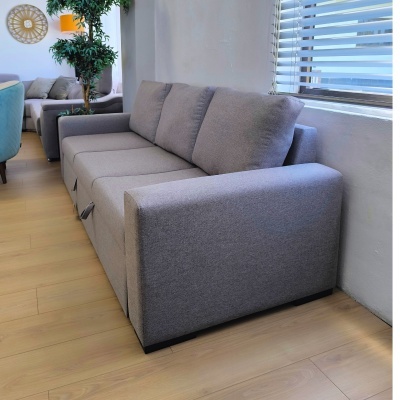 Sofá cinzento de tecido numa sala com chão de madeira clara e janela com persianas