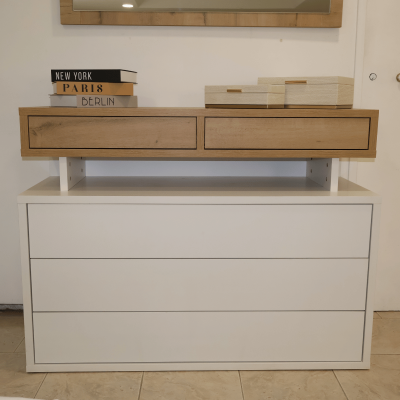 Cômoda branca com gavetas e estrutura superior em madeira natural, livros e caixas decorativas no topo