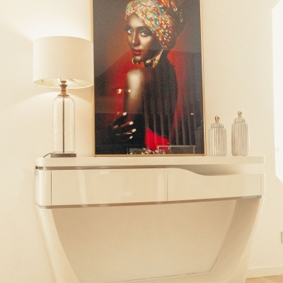 Consola branca moderna com candeeiro de base transparente e fotografia emoldurada de mulher com turbante