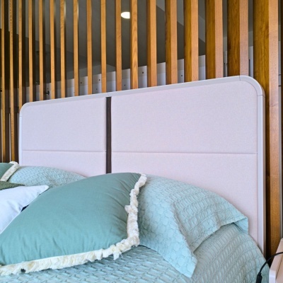 Cabeceira de cama estofada bege com roupa de cama verde e ripas de madeira ao fundo