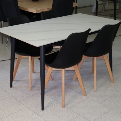 Mesa retangular branca com padrões cinzentos e quatro cadeiras pretas com pés de madeira clara em piso cinzento