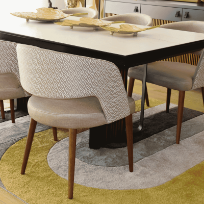Mesa de jantar com tampo branco, cadeiras estofadas bege com padrão geométrico branco, prato decorativo dourado e tapete colorido.