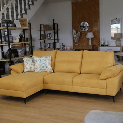 Sofá amarelo em L com almofadas florais em sala com chão de madeira e estantes