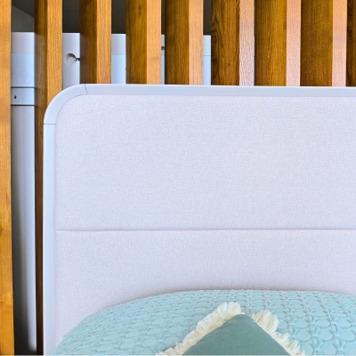 Cabeceira de cama estofada cinza claro com painel de madeira e roupa de cama azul e almofada verde