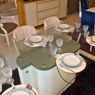 Mesa de jantar com tampo de vidro, cadeiras estofadas, conjunto de pratos e copos, em ambiente interior