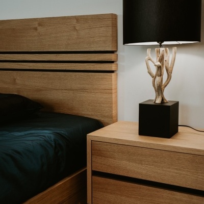 Quarto com cama e mesa de cabeceira em madeira clara, candeeiro com base decorativa e cúpula preta