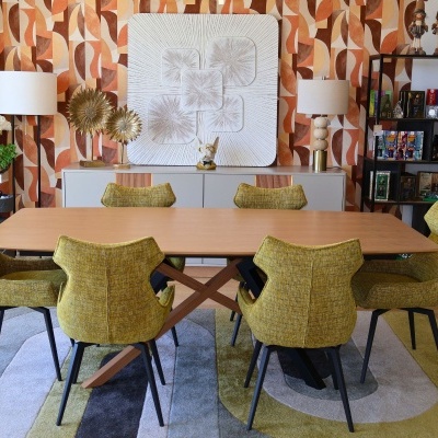 Mesa de jantar com seis cadeiras amarelas em sala com papel de parede geométrico em tons quentes