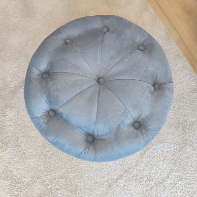 Pufe redondo cinza com botões sobre tapete bege