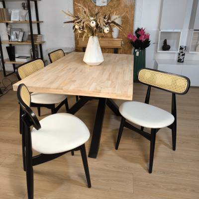 Mesa de madeira clara com cadeiras pretas com assento branco e encosto em palhinha em ambiente interior