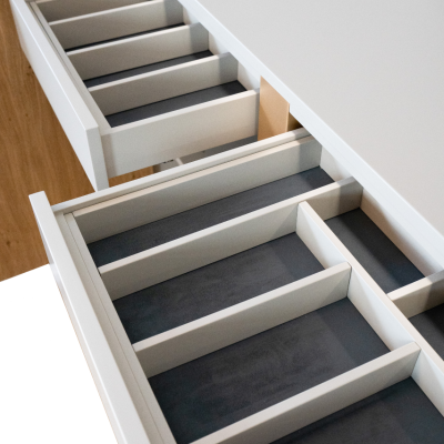 Gavetas brancas com divisórias internas e base cinza escuro encastradas numa estrutura de madeira clara