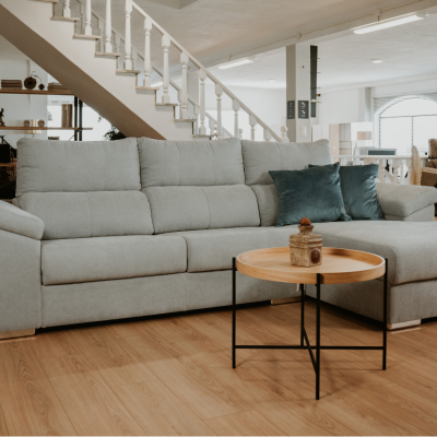 Sofá chaise longue cinzento claro com almofadas azul-petróleo e mesa de centro em ambiente interior