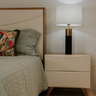 Cama com cobertor cinza, almofada decorativa, mesa de cabeceira bege com candeeiro branco