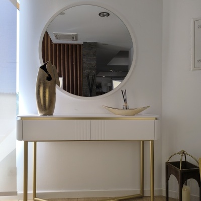 Consola branca e dourada com vaso, espelho redondo e lanterna com vela ao lado