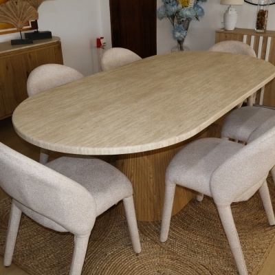 Mesa de jantar oval em pedra clara com cadeiras estofadas beige em tapete de palha, interior com móveis de madeira