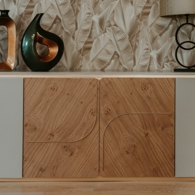 Aparador em madeira clara com esculturas e candeeiro em cima, frente a parede texturada