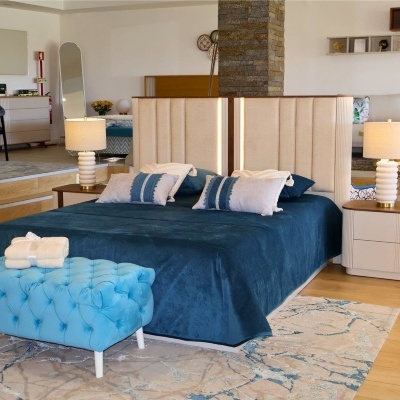 Quarto com cama azul e cabeceira bege com mesinhas de cabeceira e banco azul turquesa