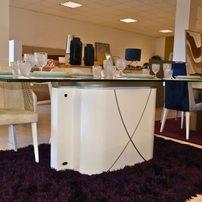 Mesa de jantar de vidro com base branca e cadeiras coloridas em sala interior