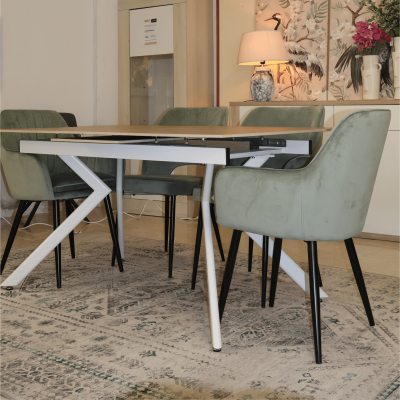 Mesa de jantar com quatro cadeiras verdes em veludo, sobre tapete cinza com padrão geométrico, com móvel decorativo ao fundo