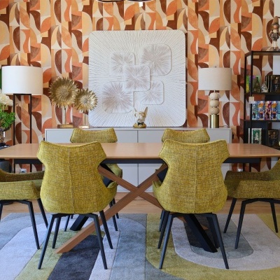Mesa de jantar com cadeiras amarelas e tapete geométrico num ambiente decorado com parede padrão geométrico laranja e móveis decorativos.