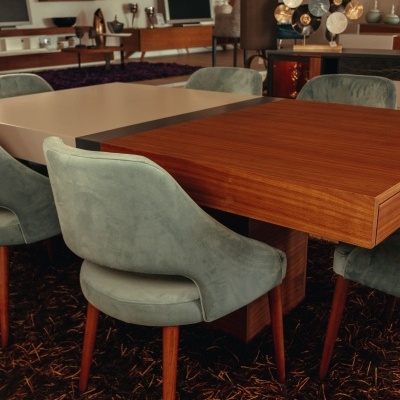 Sala com mesa de madeira e cadeiras estofadas verdes, tapete preto com linhas castanhas e móveis de madeira