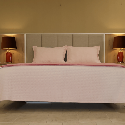 Cama casal com cabeceira estofada bege, roupa de cama rosa, e 2 candeeiros vermelhos com abat-jours castanhos