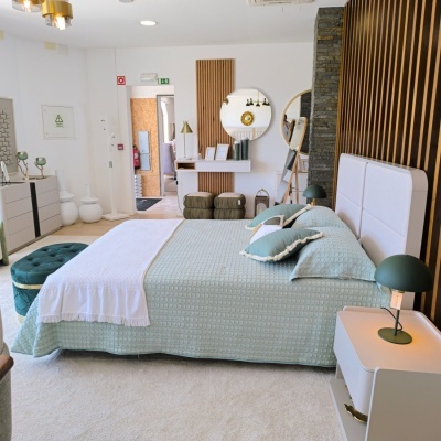 Quarto com cama estofada branca, colcha verde água, almofadas, mesas de cabeceira, candeeiros verde escuro e decor com ripado de madeira