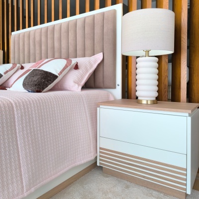 Cabeceira estofada bege de cama, cama com roupa de cama rosa e almofadas decorativas, mesa de cabeceira branca com candeeiro de base ondulada perto de parede com ripas de madeira