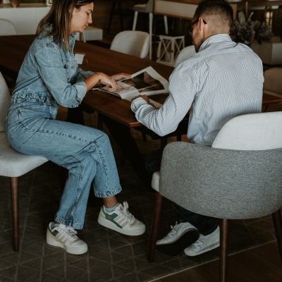 Duas pessoas sentadas a ler um livro numa mesa de madeira