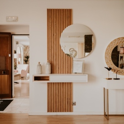 Sala interior com espelhos redondos, parede em pedra e móveis brancos.