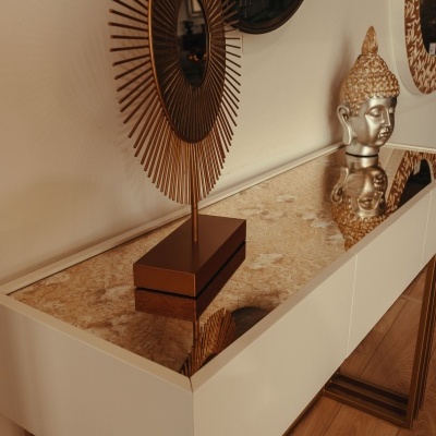 Consola branca com tampo espelhado dourado e decoração com estátua de Buda e objeto metálico circular dourado