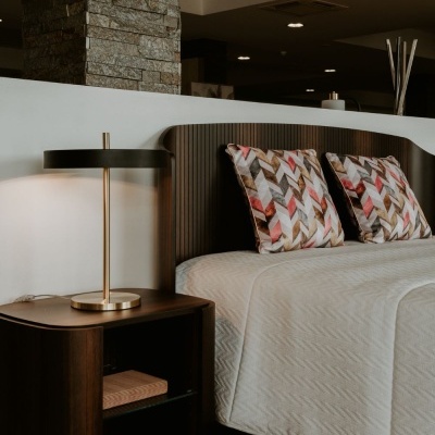 Mesa de cabeceira de madeira escura ao lado de cama com cabeceira canelada e almofadas coloridas.