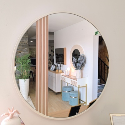 Espelho redondo branco refletindo sala com móvel branco, pufes azuis, vaso com plantas e parede branca