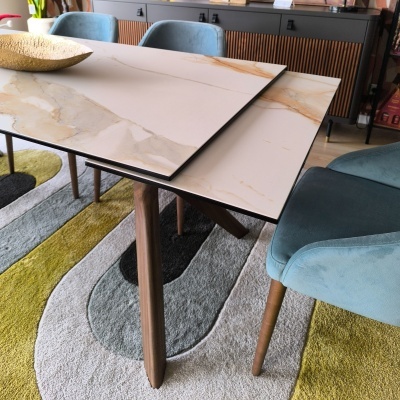 Mesa extensível com tampo bege estilo mármore e pés de madeira, cadeiras azul claro, tapete geométrico colorido