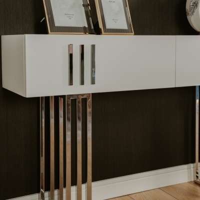 Móvel de parede branco com puxadores metálicos e pernas metálicas contra parede escura
