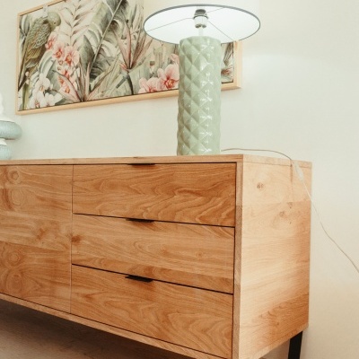 Aparador de madeira clara com candeeiro verde e quadro decorativo de folhas tropicais