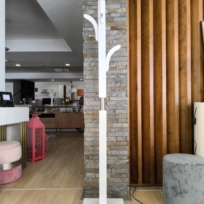 Cabide de pé branco em interior ao lado de pufe cinza e parede decorativa